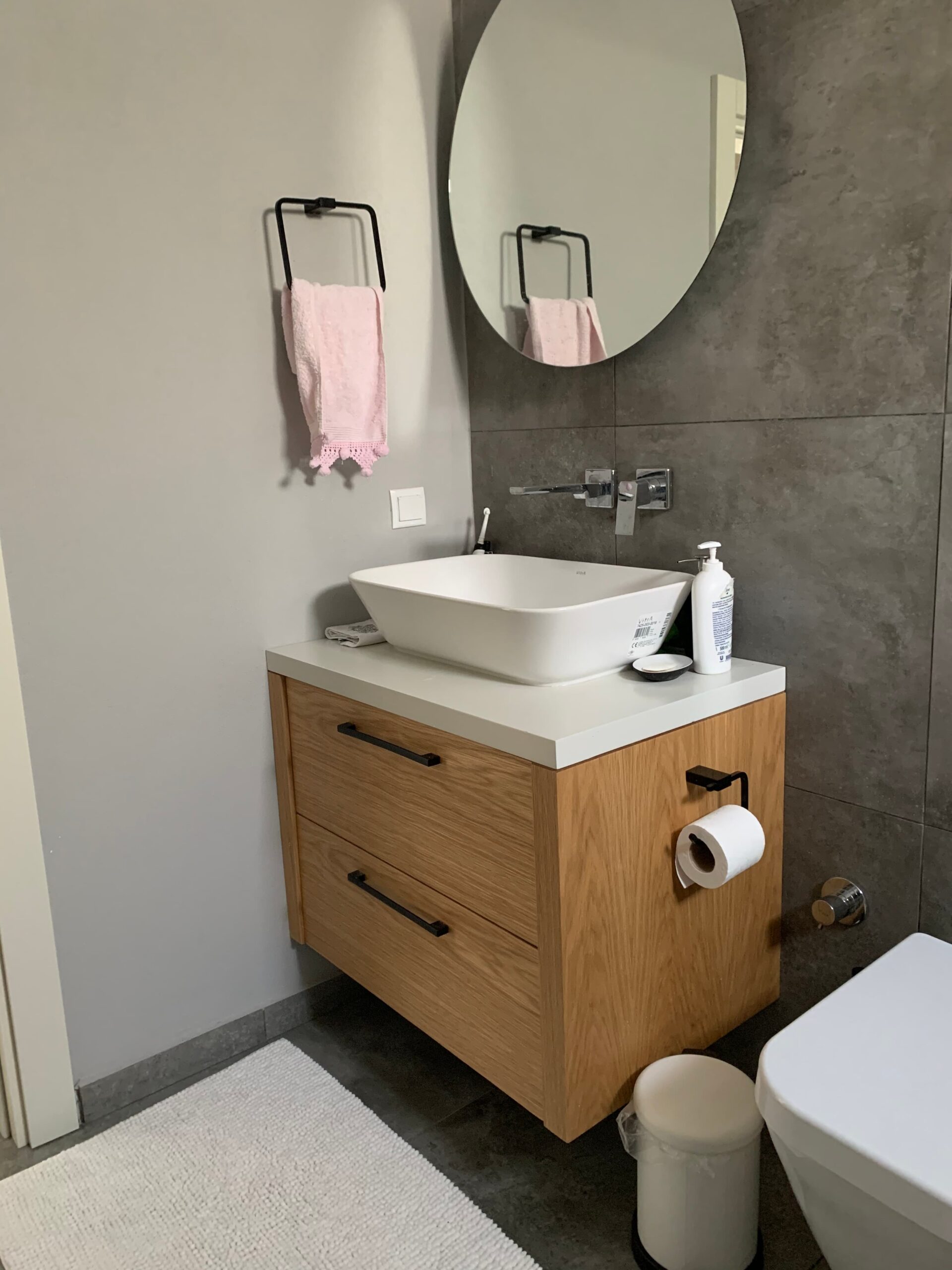 Yuvarlak aynası, modern lavabosu ve ahşap dolabıyla, tamamlanmış banyo projesinin gerçek fotoğrafı.